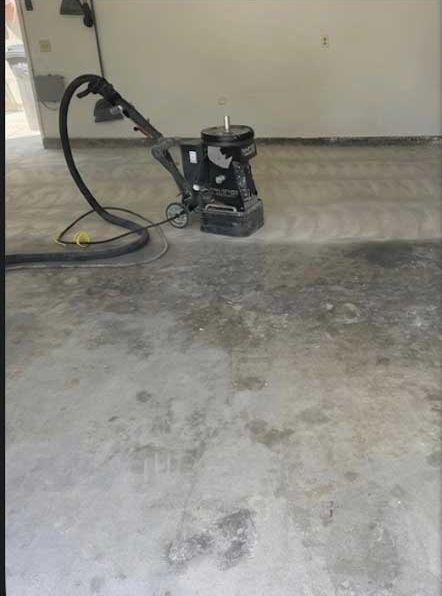 A walk-behind diamond grinder with its dust hose, part way across a stained garage slab.