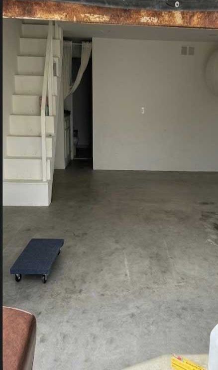 A bare grey concrete slab in an unfinished garage, stained and marked, with a stair and a dolly beside it.