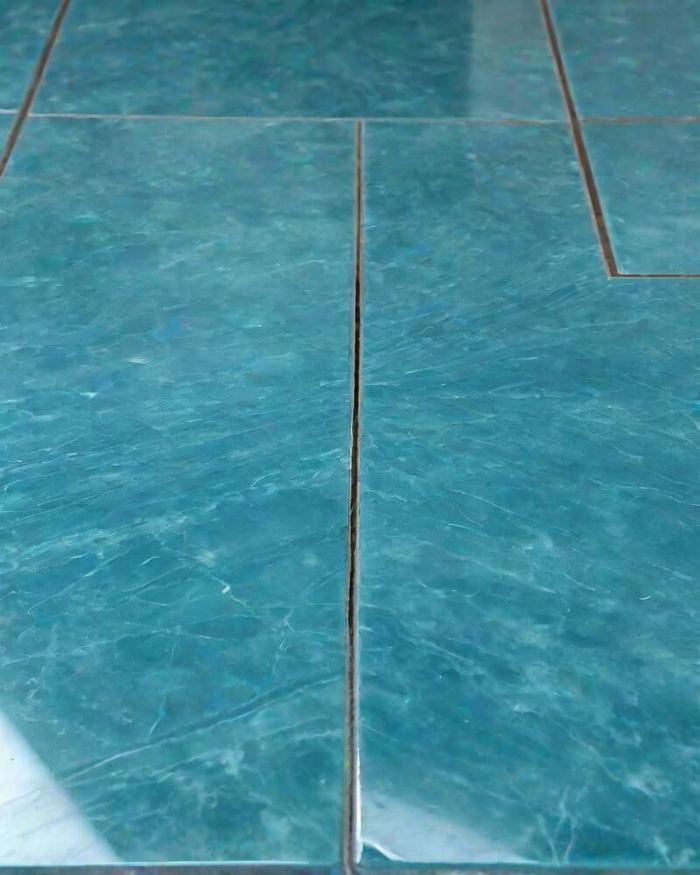 Close view of a high-gloss teal resin floor with a mirror-bright reflection along the edge.